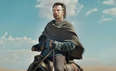 Obi-Wan Kenobi in desert attire rides a creature under a blue sky with scattered clouds.