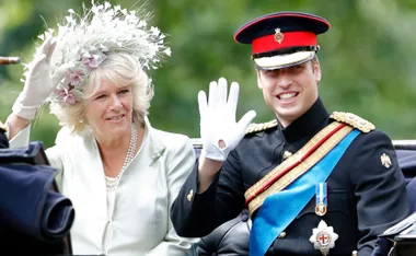 Two individuals in formal attire wave during a carriage procession.