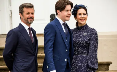 Royal family members smiling, all dressed in formal attire, stand outside near stairs.
