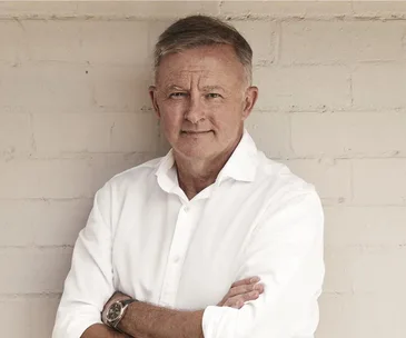 Australian Prime Minister Anthony Albanese in a white shirt against a brick wall.