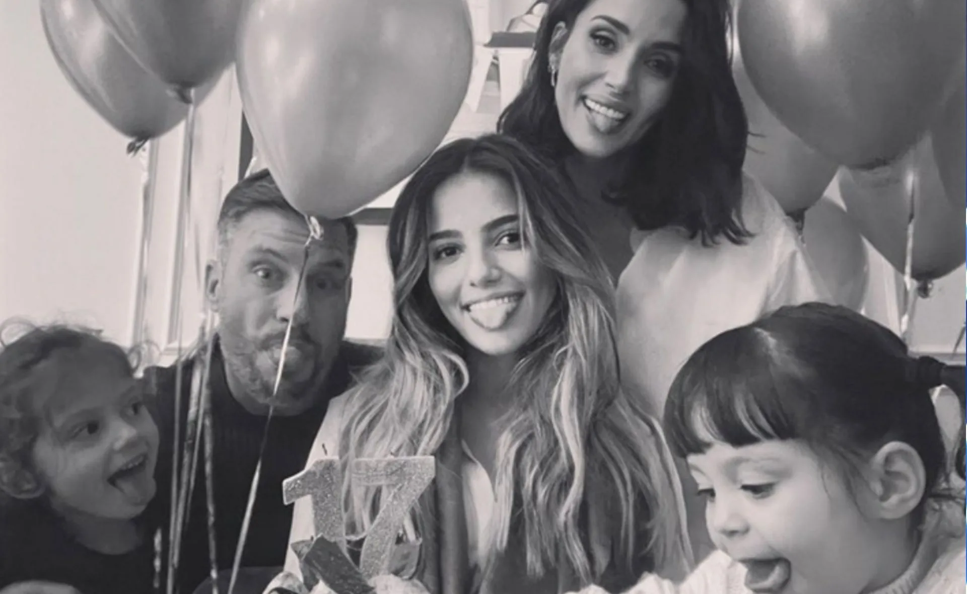 A family celebrates a birthday with smiles, balloons, and a cake with the number 17.