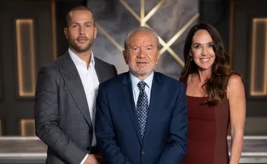 Three individuals standing together, dressed in formal attire, with a blurred background.