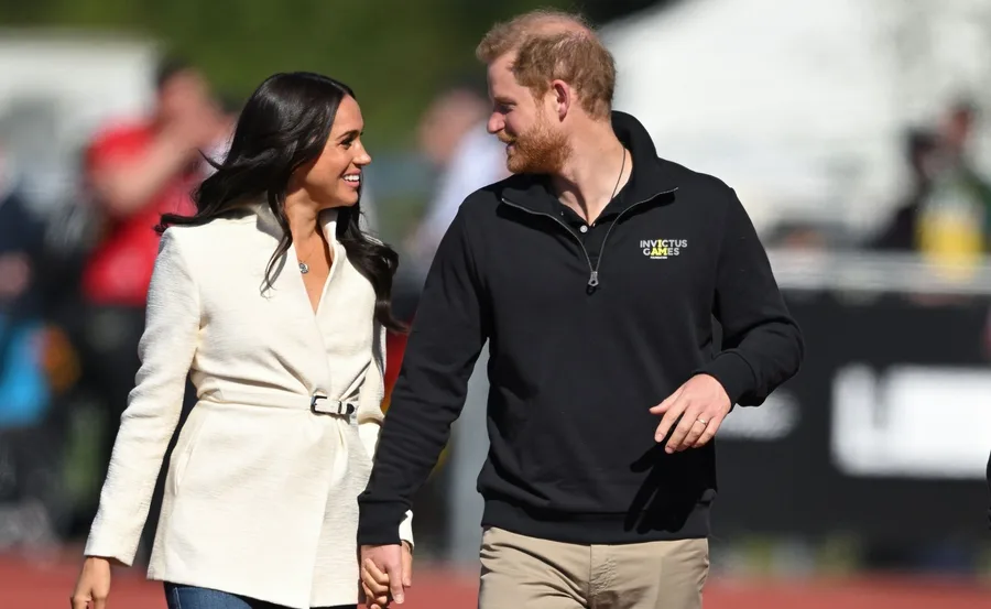 A couple holding hands and smiling at each other outdoors in a casual setting.