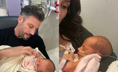 A father and mother each holding a newborn baby in a hospital setting, baby with medical tubes.