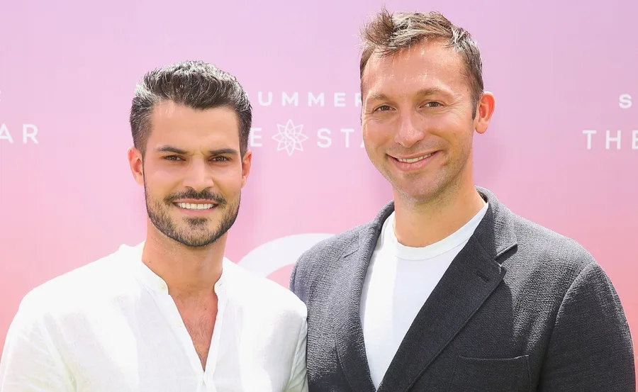 Two men smiling at an outdoor event with a pink background.