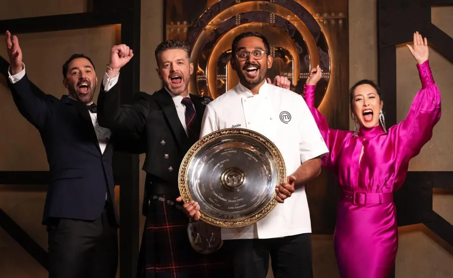 Four people celebrate, one holding a large MasterChef trophy in a chef coat with "Justin" printed on it.