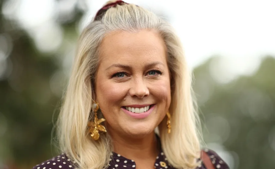 Smiling woman with blonde hair, wearing polka dot outfit and gold earrings, in an outdoor setting.