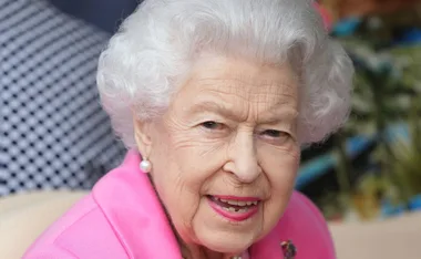 Elderly woman with white hair and a pink outfit, smiling at the camera.
