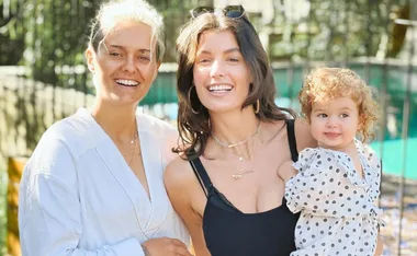 Smiling group of three, two adults and a baby in polka dot outfit, in sunny outdoor setting.