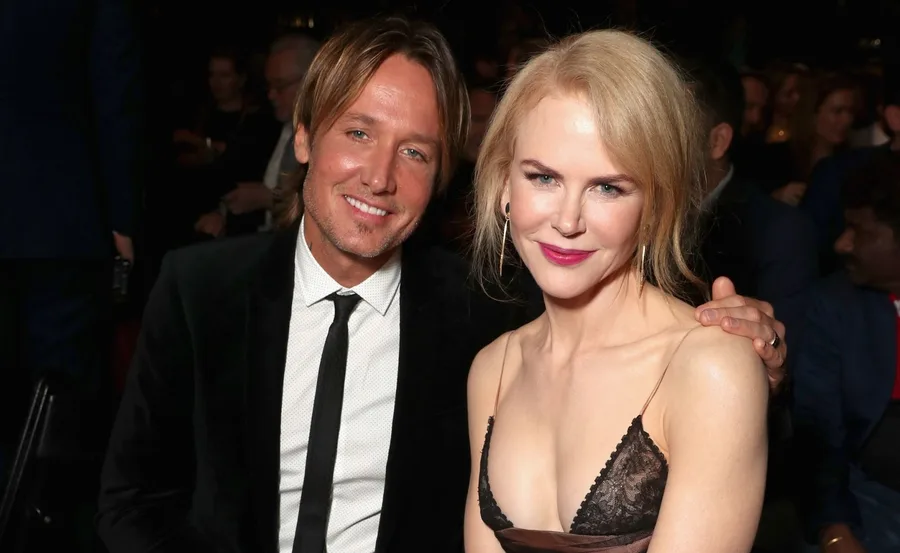 A couple posing and smiling in formal attire at an event, surrounded by a dimly lit audience.