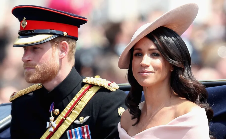 Prince Harry in uniform and Meghan Markle in a pink dress and hat at a public event.