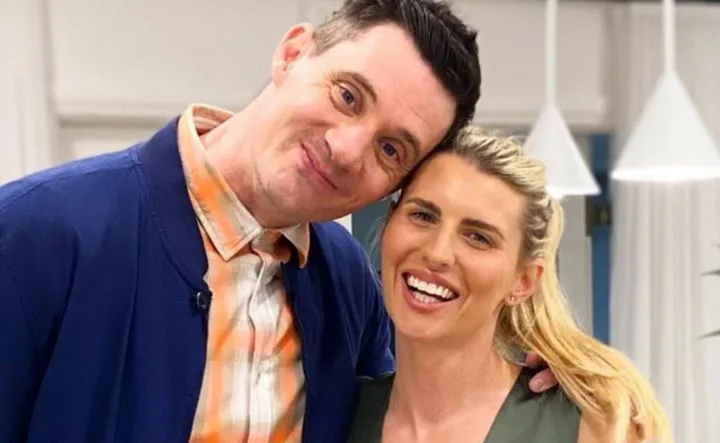 Man in blue jacket and woman in green top smiling together indoors.