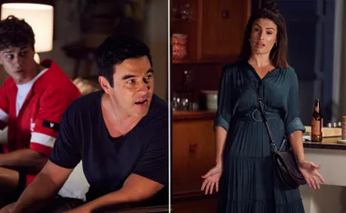Characters in a heated discussion in a living room; one standing, two seated, with a bottle on the counter nearby.
