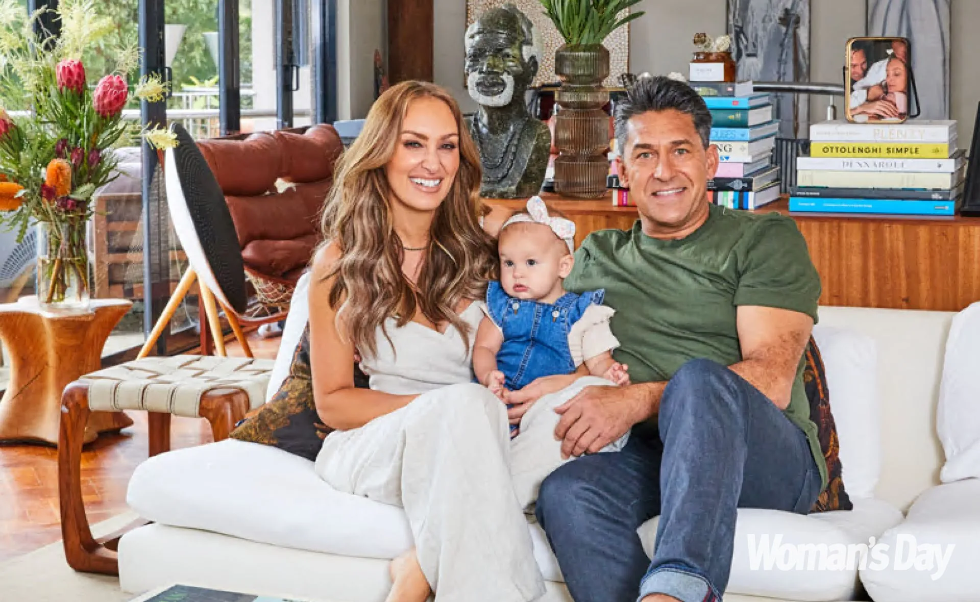 Family sitting on a sofa in a cozy living room, smiling at the camera, with books and decor in the background.