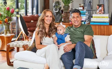Family sitting on a sofa in a cozy living room, smiling at the camera, with books and decor in the background.