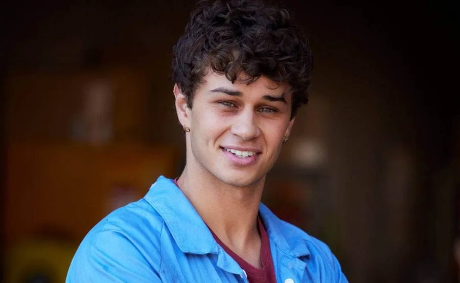 Young man with curly hair in a blue shirt smiling warmly at the camera.