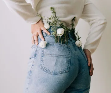 Woman in blue jeans with white flowers in pockets, hands on hips.