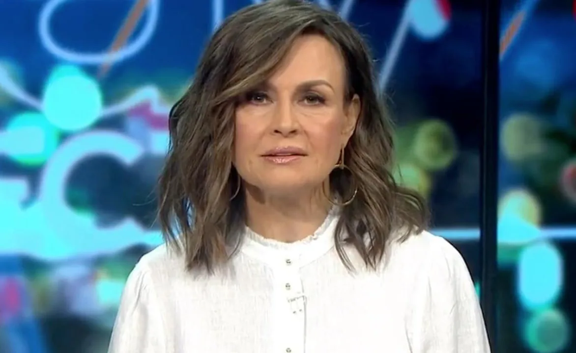 A woman with shoulder-length hair in a white top, with a blurred colorful background.