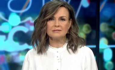 A woman with shoulder-length hair in a white top, with a blurred colorful background.