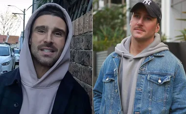 Two men outdoors wearing casual hoodies and jackets; one with a cap and the other with a hood up.