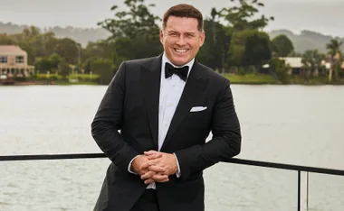 A person in a tuxedo smiling in front of a scenic riverside background.