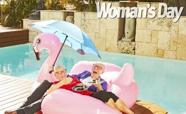 Elderly couple enjoying cake on pink flamingo float in pool with blue umbrella, smiling at each other.