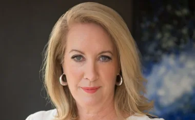 Portrait of Elizabeth Broderick, a professional woman with blonde hair, wearing hoop earrings, and a white top.