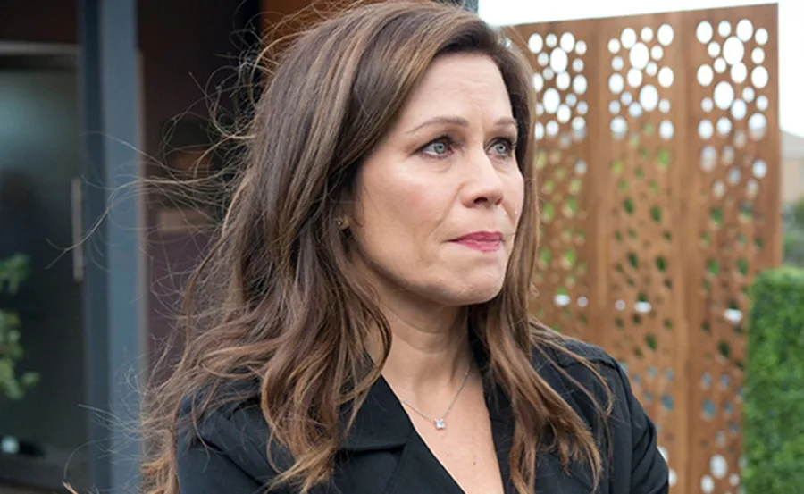 Woman with long brown hair in black top stands outdoors, looking concerned.
