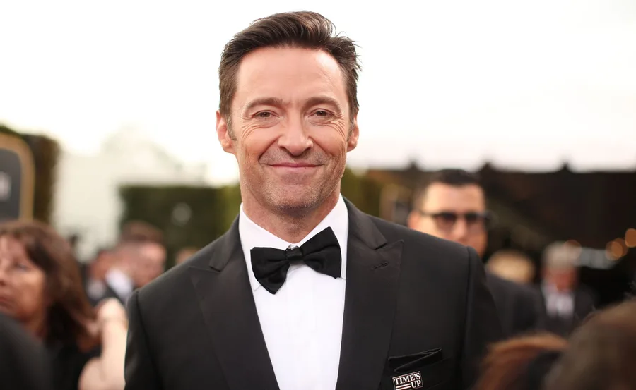 Man in a tuxedo smiling at a formal event with people blurred in the background.