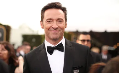 Man in a tuxedo smiling at a formal event with people blurred in the background.