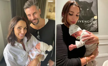 Couple smiling, holding a baby wrapped in floral blanket; woman cuddling baby with pacifier, against Givenchy poster.