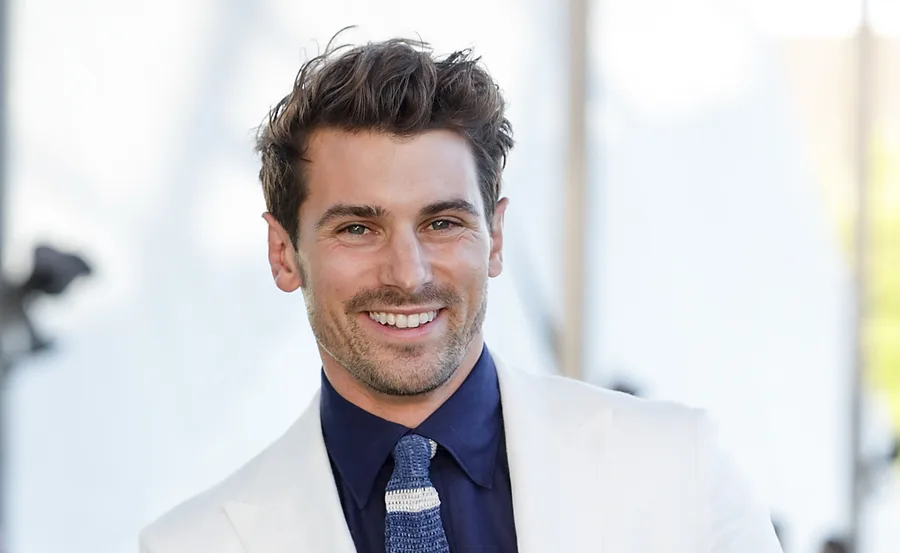 Smiling man in a white suit and blue tie at an outdoor event.