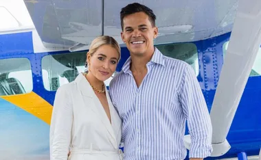 Couple standing together, smiling in front of a small blue and yellow airplane.