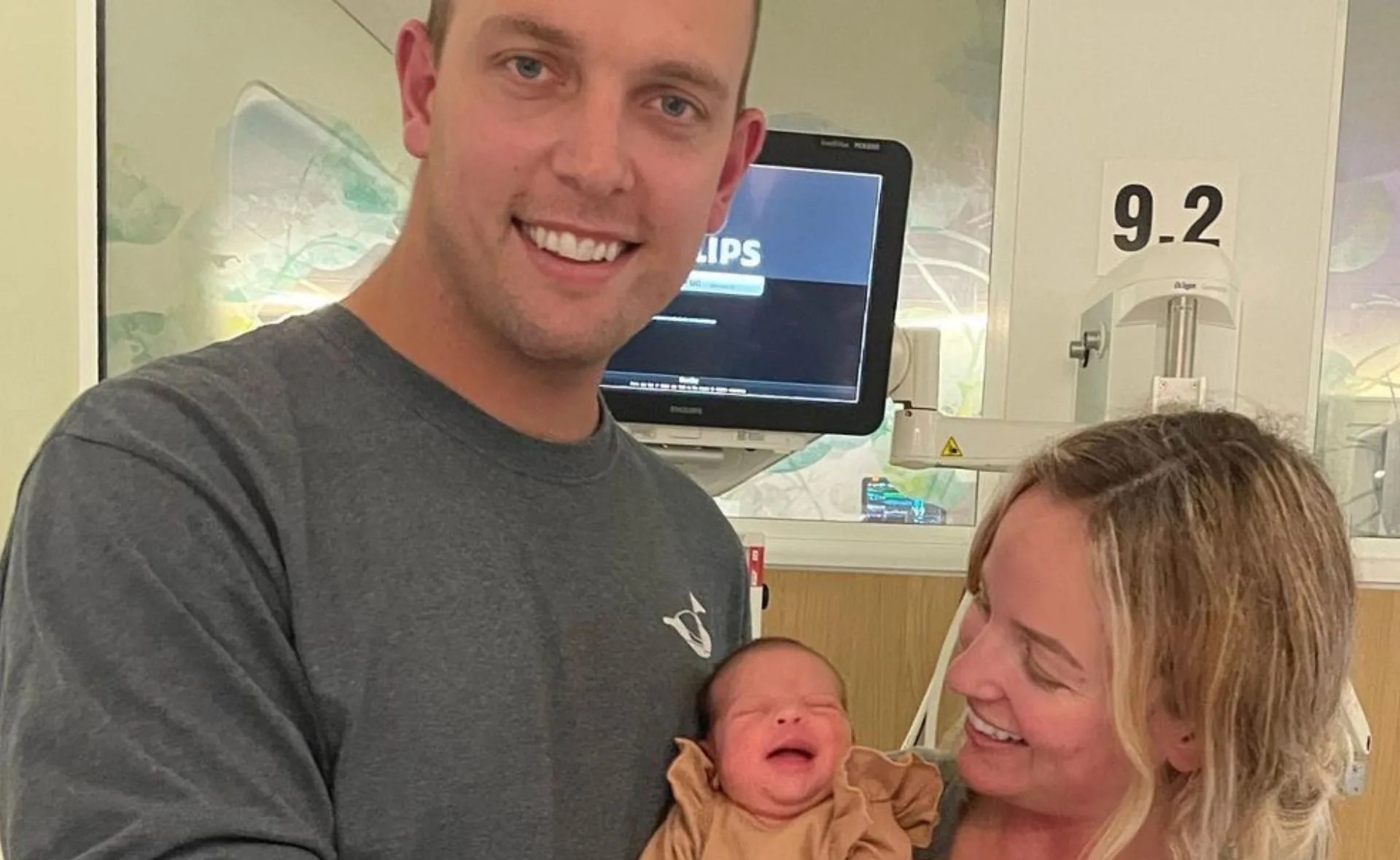 Man and woman smiling at a newborn baby in a hospital setting.