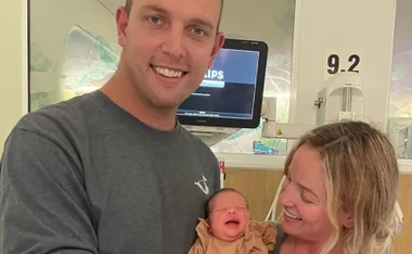 Man and woman smiling at a newborn baby in a hospital setting.
