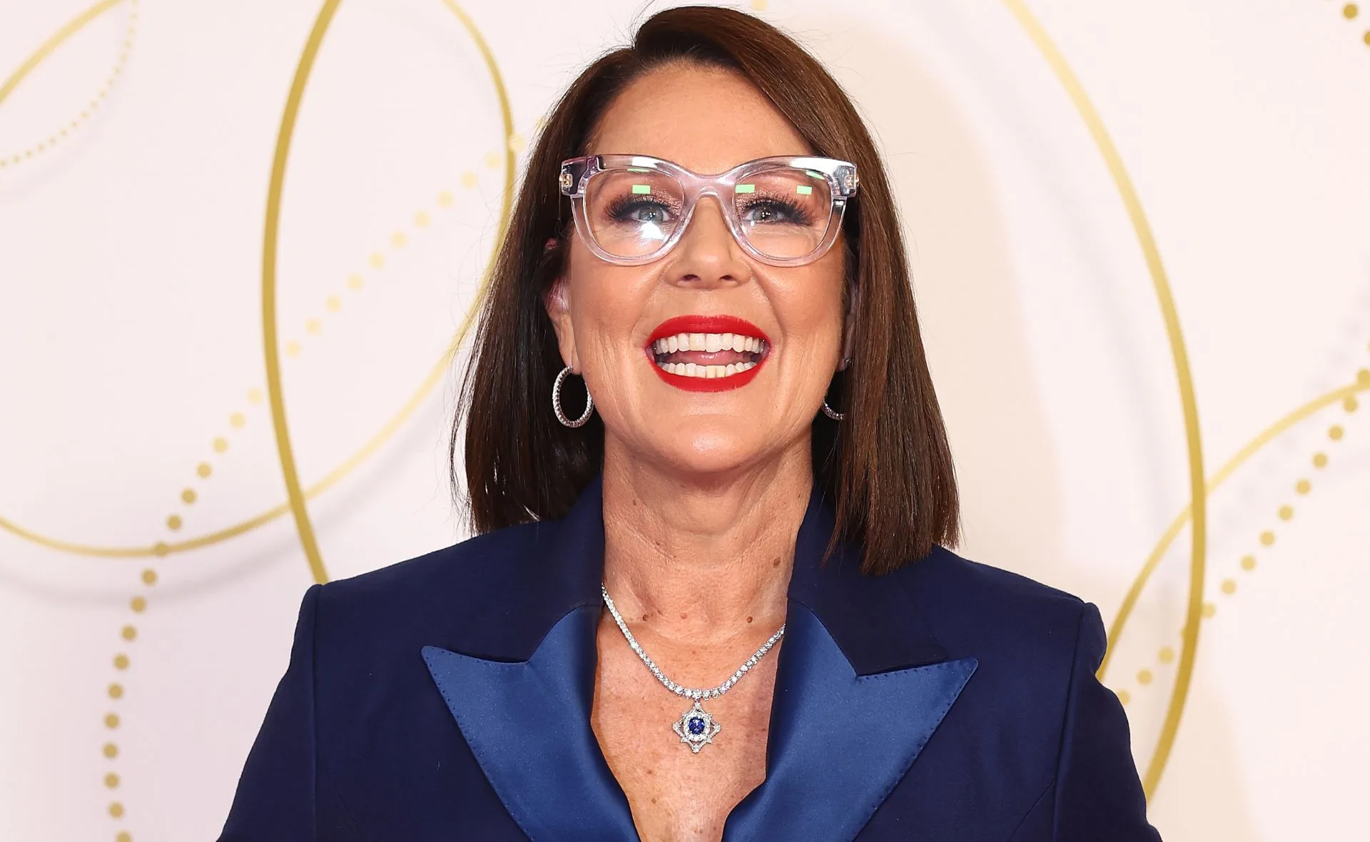 Person smiling in glasses, wearing a blue outfit and a necklace, at the 2022 Logie Awards.