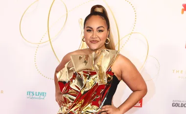 Jessica Mauboy on the red carpet in a striking gold and black dress, smiling confidently.