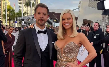 A couple in formal attire poses on the red carpet at the Logies 2022 event with a crowd in the background.