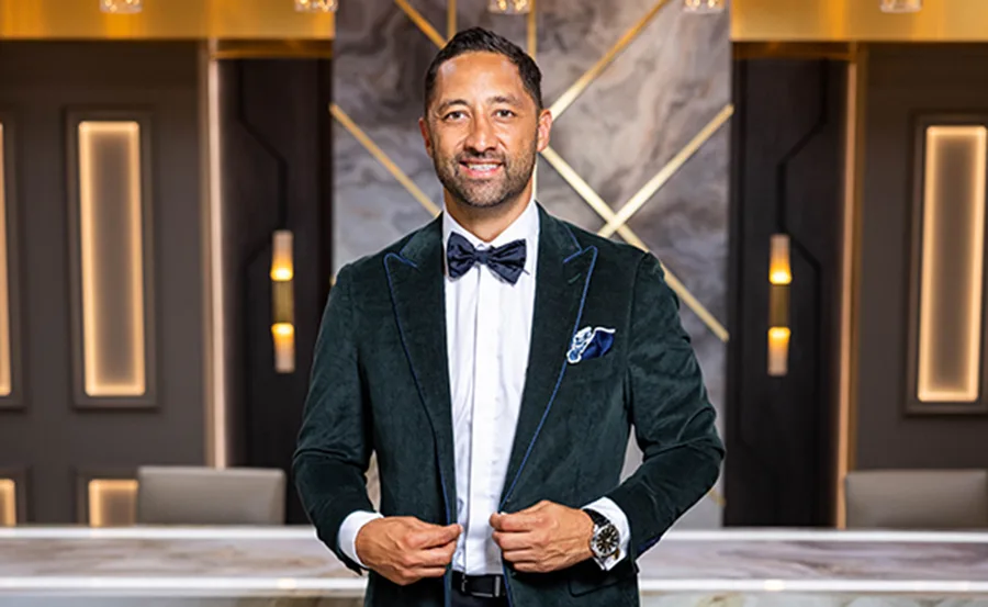 Man in a suit and bow tie stands confidently in a stylishly lit room.