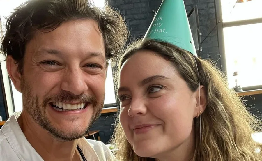 A smiling man and woman with a party hat indoors. The woman looks at him affectionately.