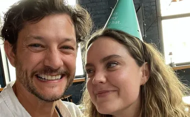 A smiling man and woman with a party hat indoors. The woman looks at him affectionately.
