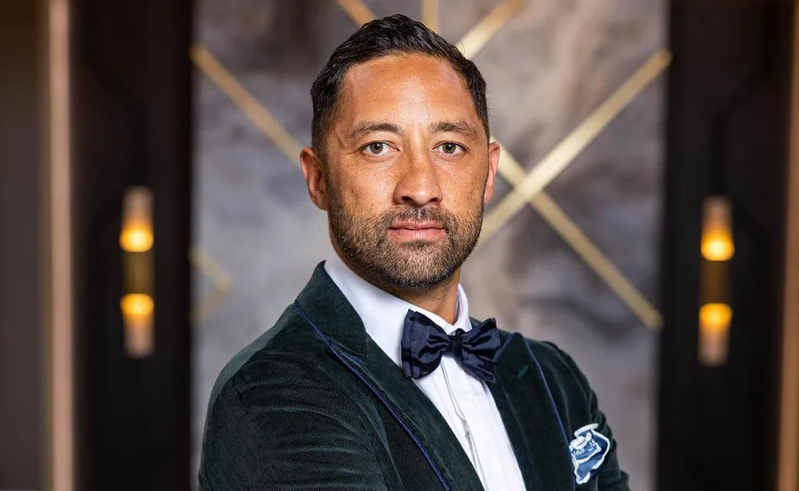 Person in a green velvet suit and bow tie, standing in front of a blurred geometric background.