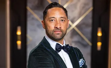 Person in a green velvet suit and bow tie, standing in front of a blurred geometric background.