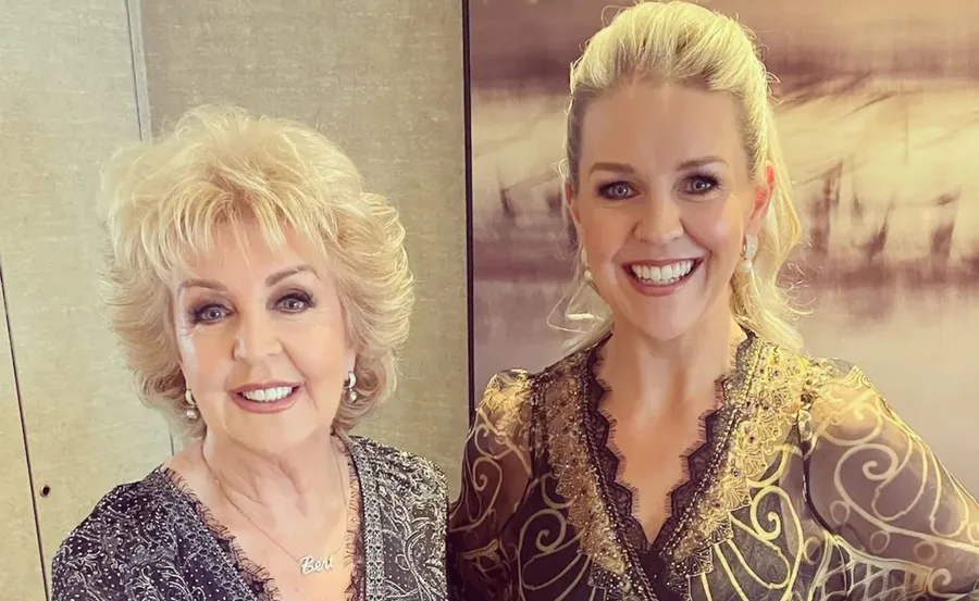 Two women smiling at the camera, dressed in intricate, elegant outfits.