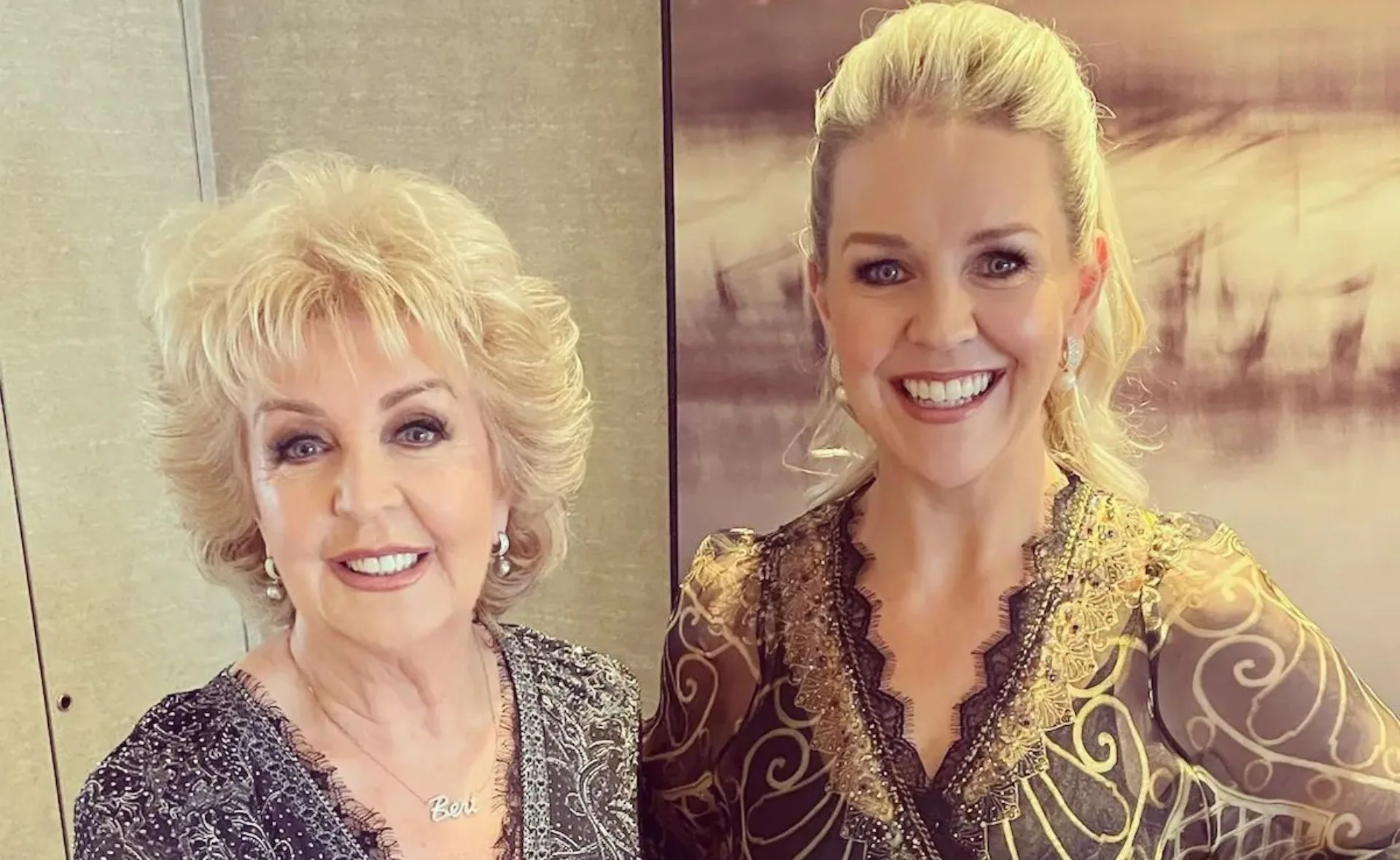Two women smiling at the camera, dressed in intricate, elegant outfits.