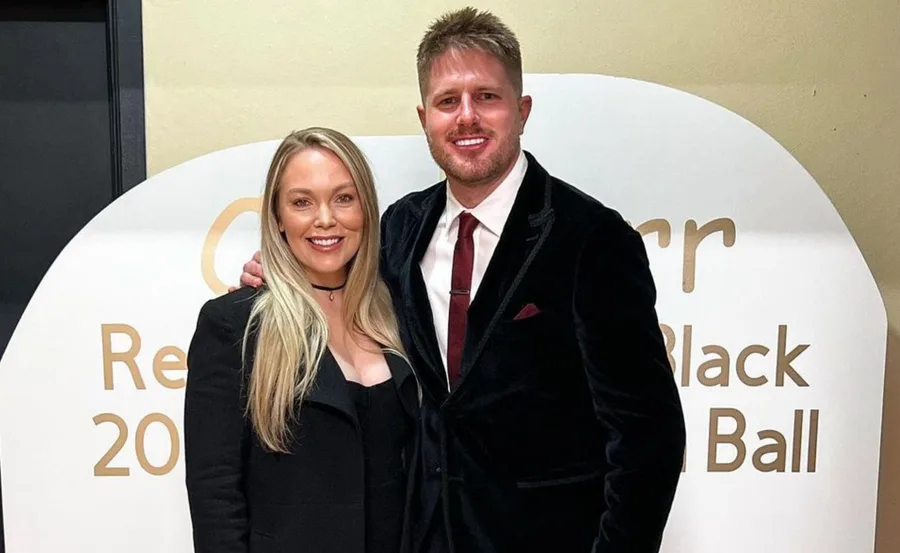 A smiling couple dressed formally, standing in front of a sign at a black tie event.