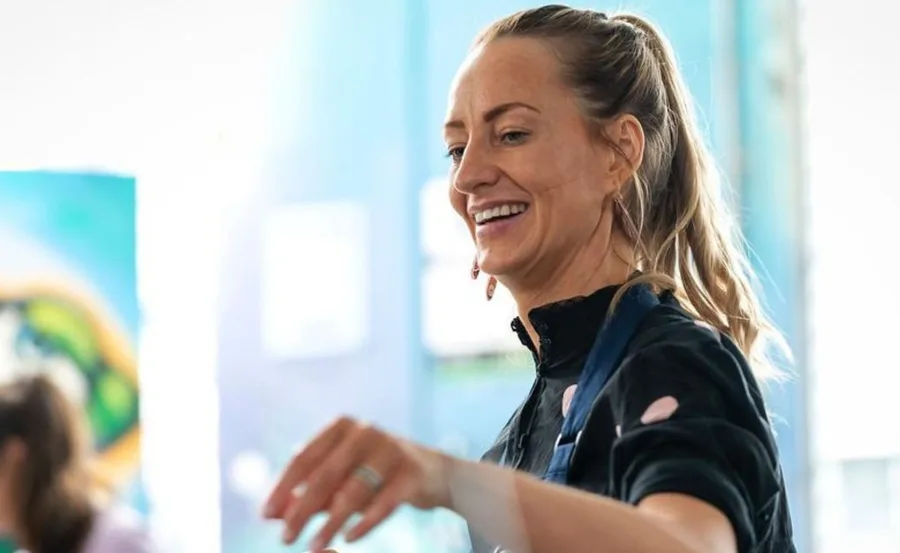 A smiling woman in a blue apron with background blur.