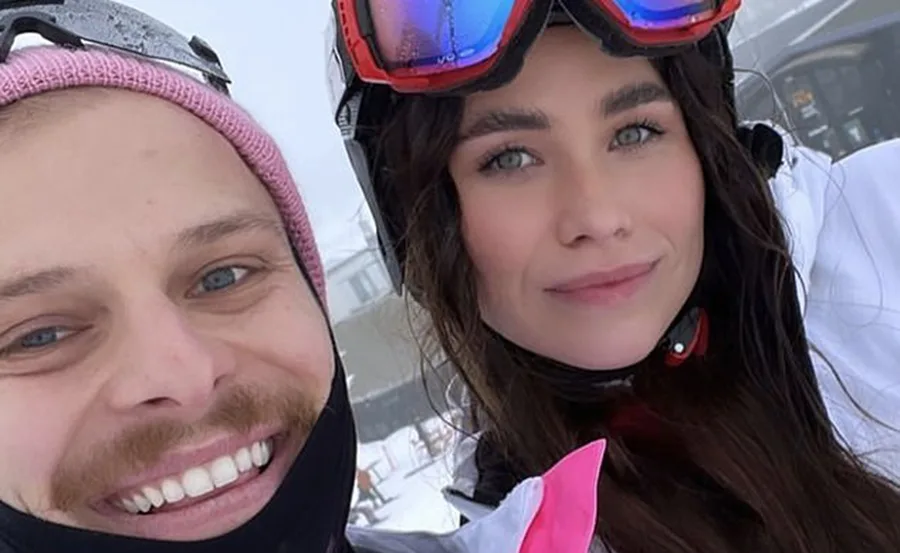 Two people taking a snowy outdoor selfie. One wears a pink beanie, the other ski goggles.