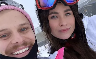 Two people taking a snowy outdoor selfie. One wears a pink beanie, the other ski goggles.