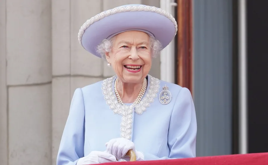 Elderly woman in a light blue outfit with a hat, smiling.